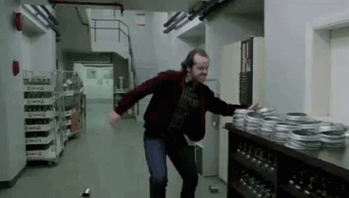 GIF from The Shining: Jack Nickolson's character Jack Torrance angrily knocks a bunch of things off a counter while walking through a corridor
