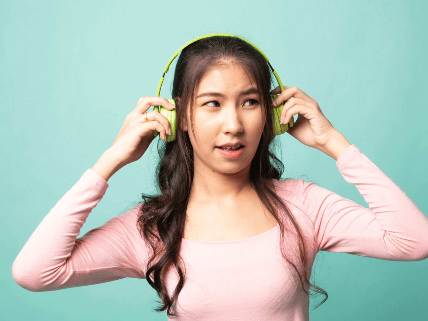 A teenager with ADHD and autism holds lime green headphones over her ears.