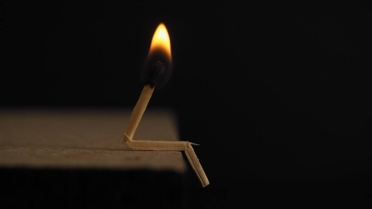A lit match broken in two places made to look like a person sitting on the edge of a table