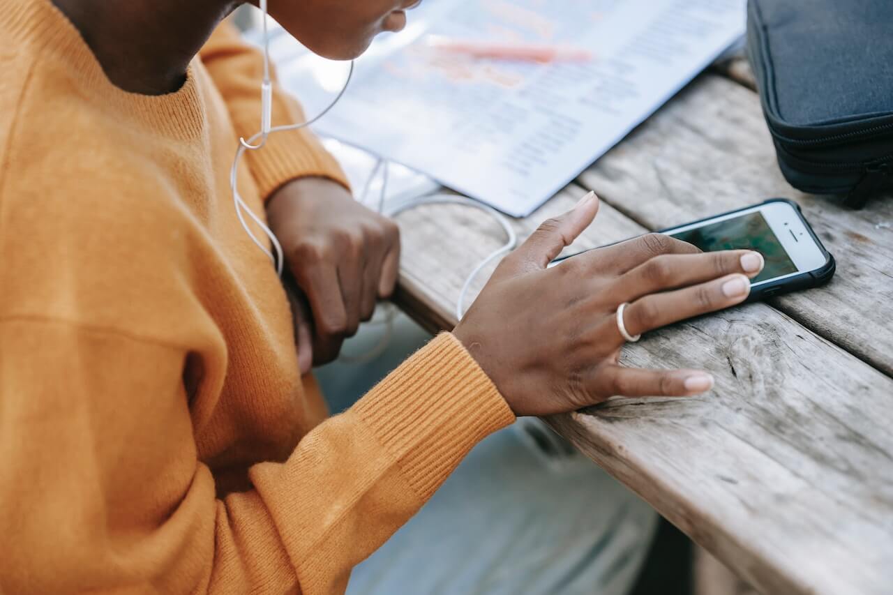 A woman listening to music from her phone and working on homework checks notifications from her phone's screen.