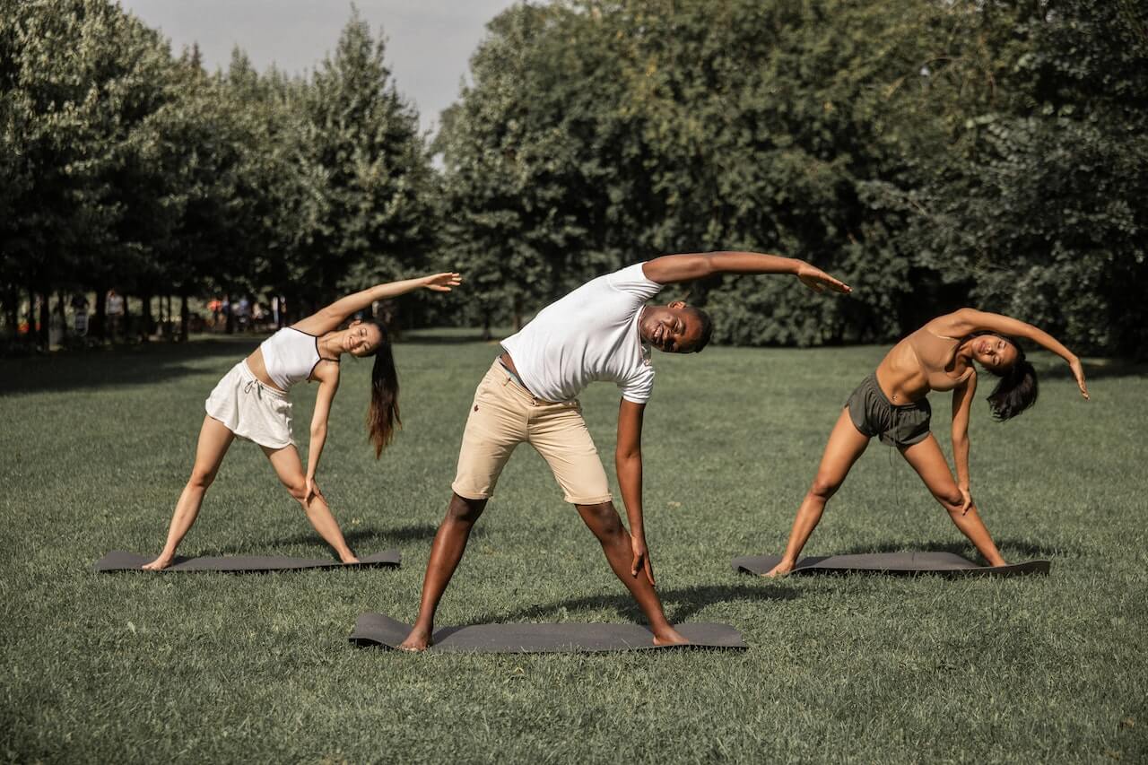 Three friends in a sunny park, doing stretching exercises on the lawn.