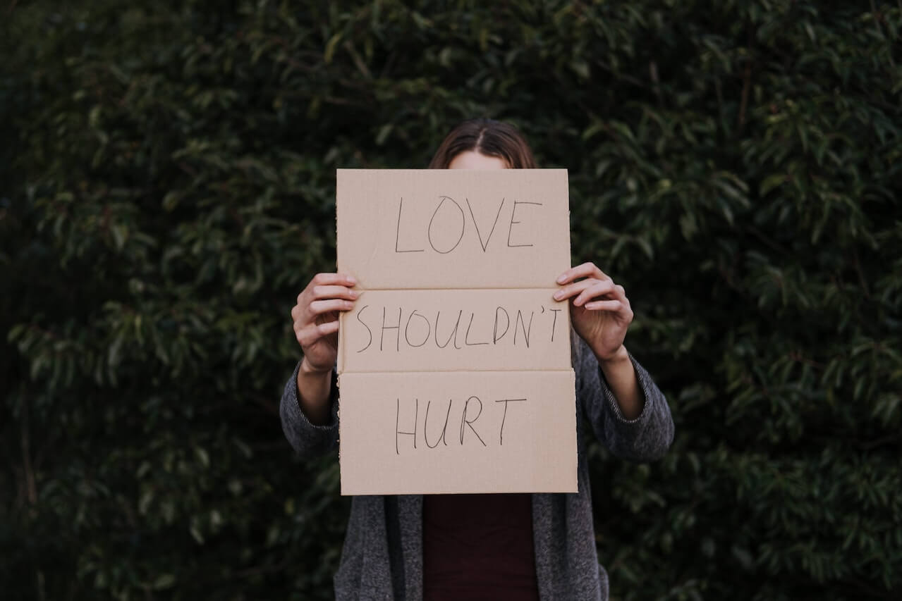 A woman holding a sign in front of her face that reads, love shouldn't hurt