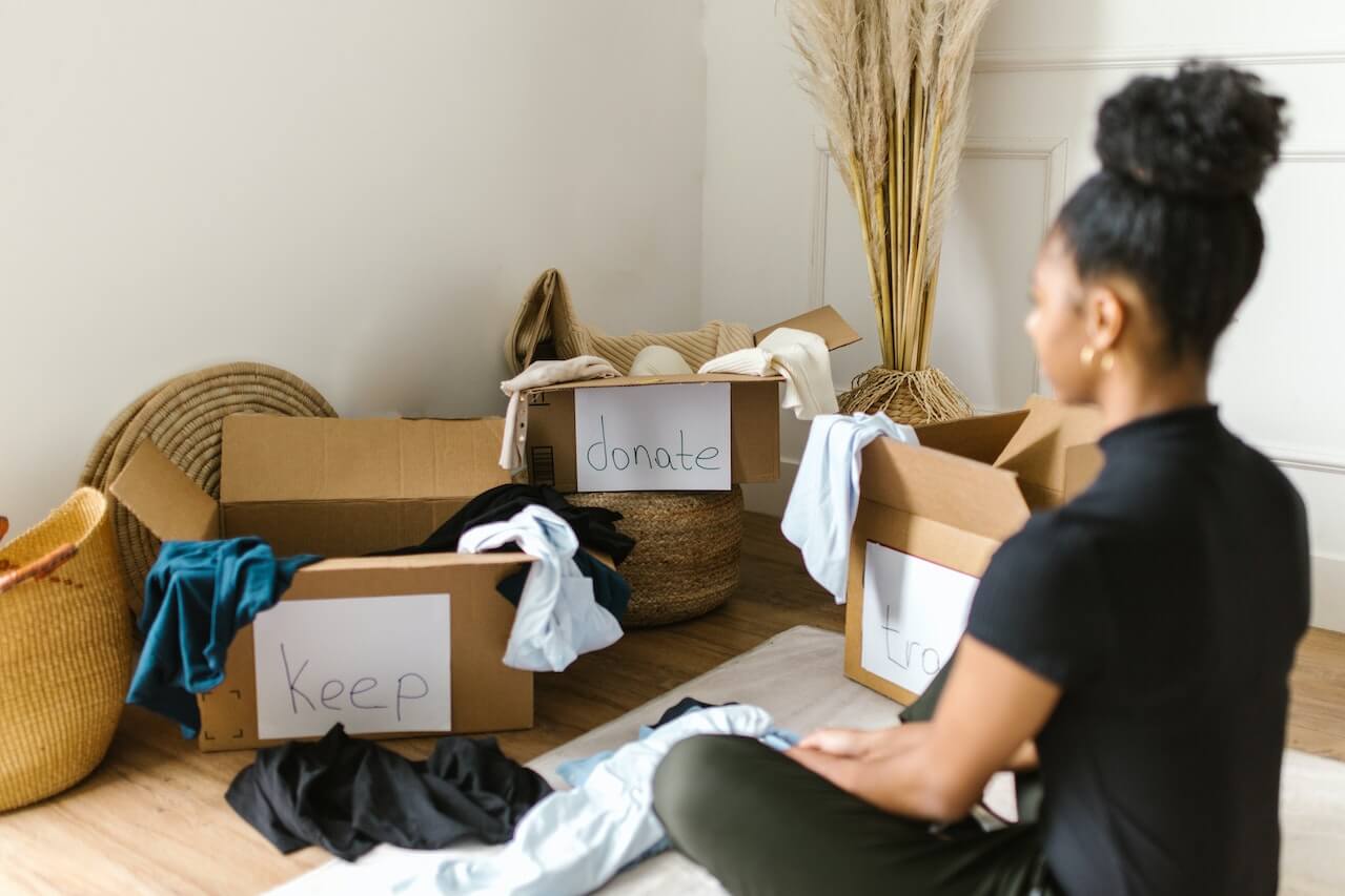 A woman with ADHD sitting in front of three boxes, trying to organize her house. The boxes read: keep, donate, and trash