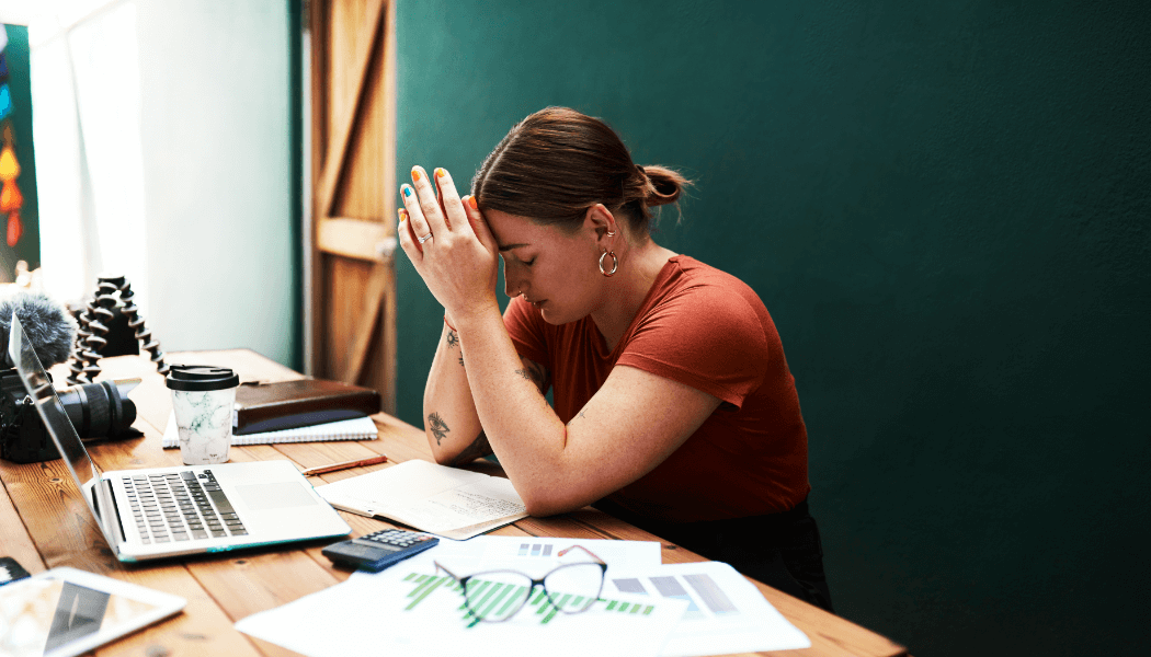 A woman with ADHD sitting at her desk unable to focus or switch tasks. Her head is resting on her hands.