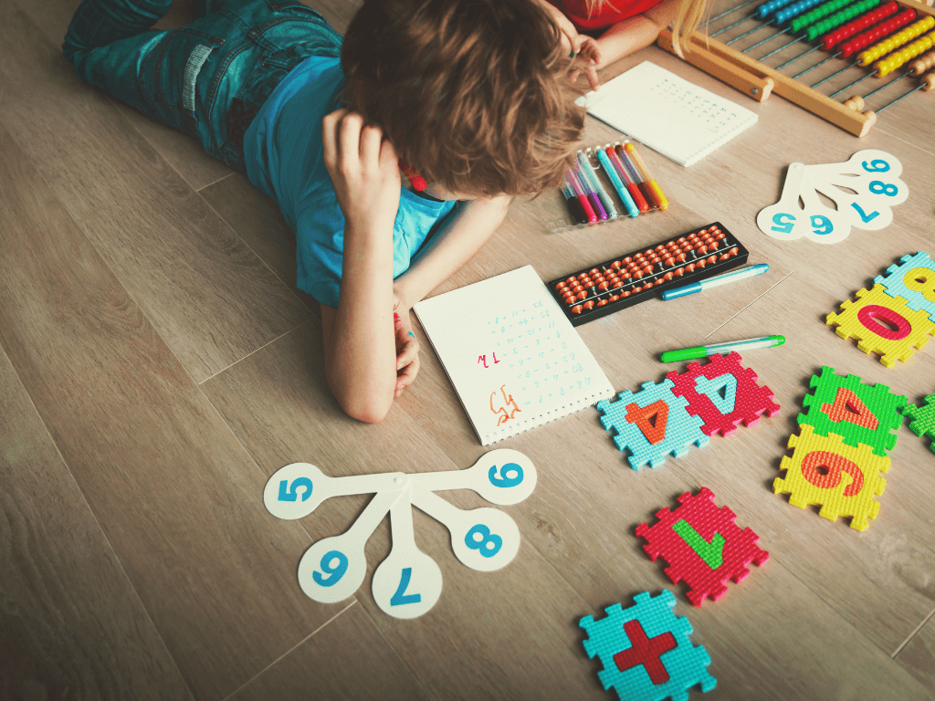 A young boy lying on the floor looking at various colorful number learning puzzles and visual aids. 