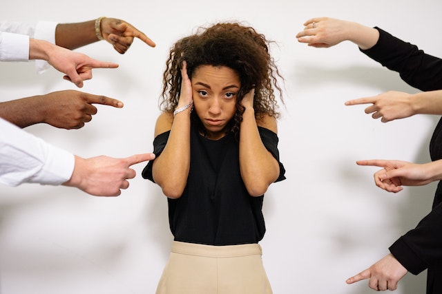 A woman holding her ears and standing in the middle of people pointing at her