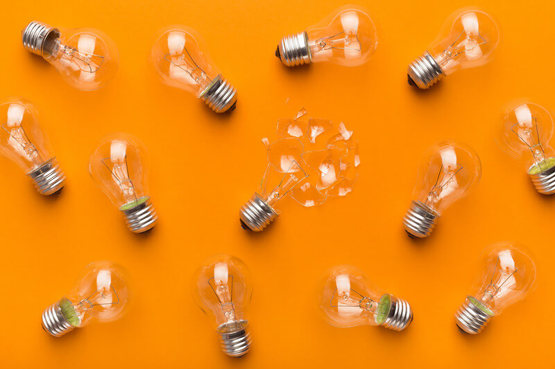 Glass lightbulbs sit on an orange background. One of the bulbs is broken.
