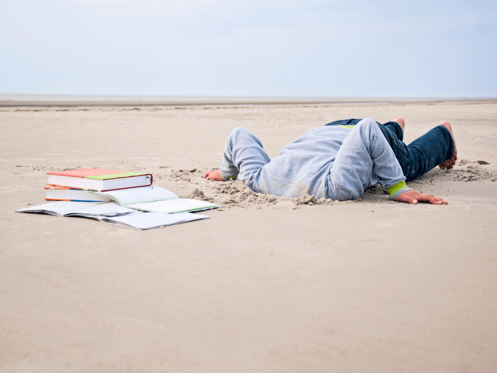 Unmotivated person with ADHD avoiding their work with their head in the sand and their books surrounding them