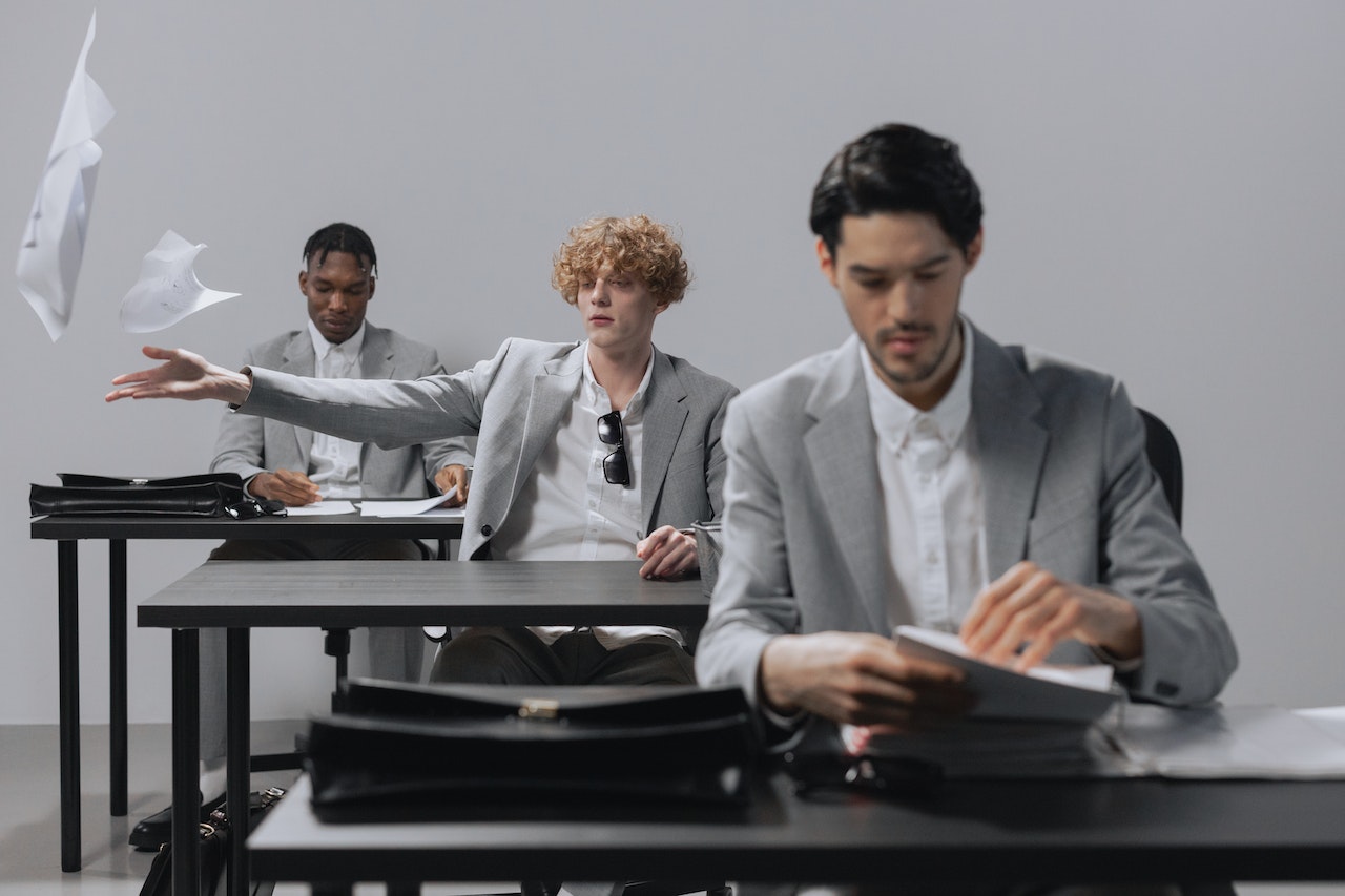 Three young office workers sitting at desks behind each other, the middle one defying authority by throwing paperwork in the air.