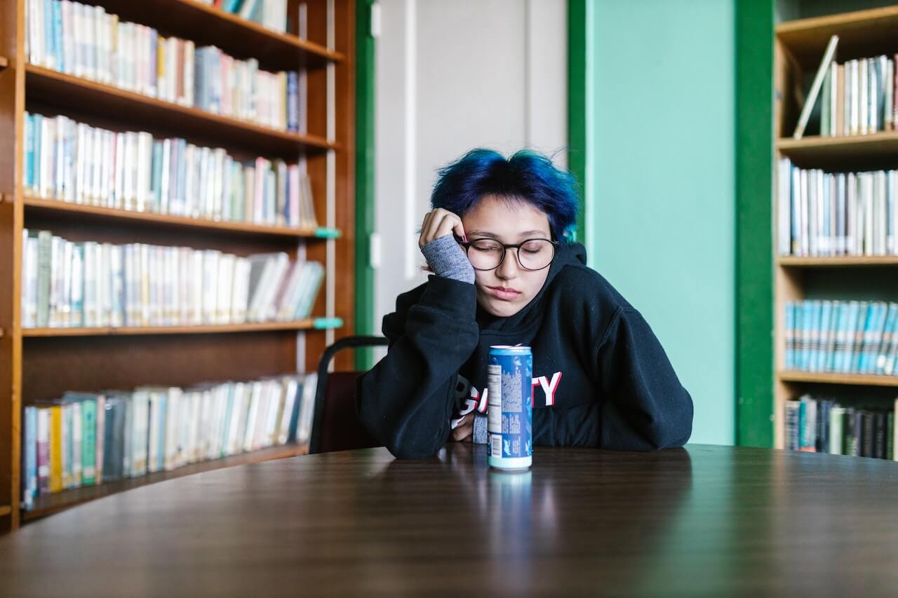 A person with ADHD is tired and falling asleep, nodding off, in a library despite having caffeine with them