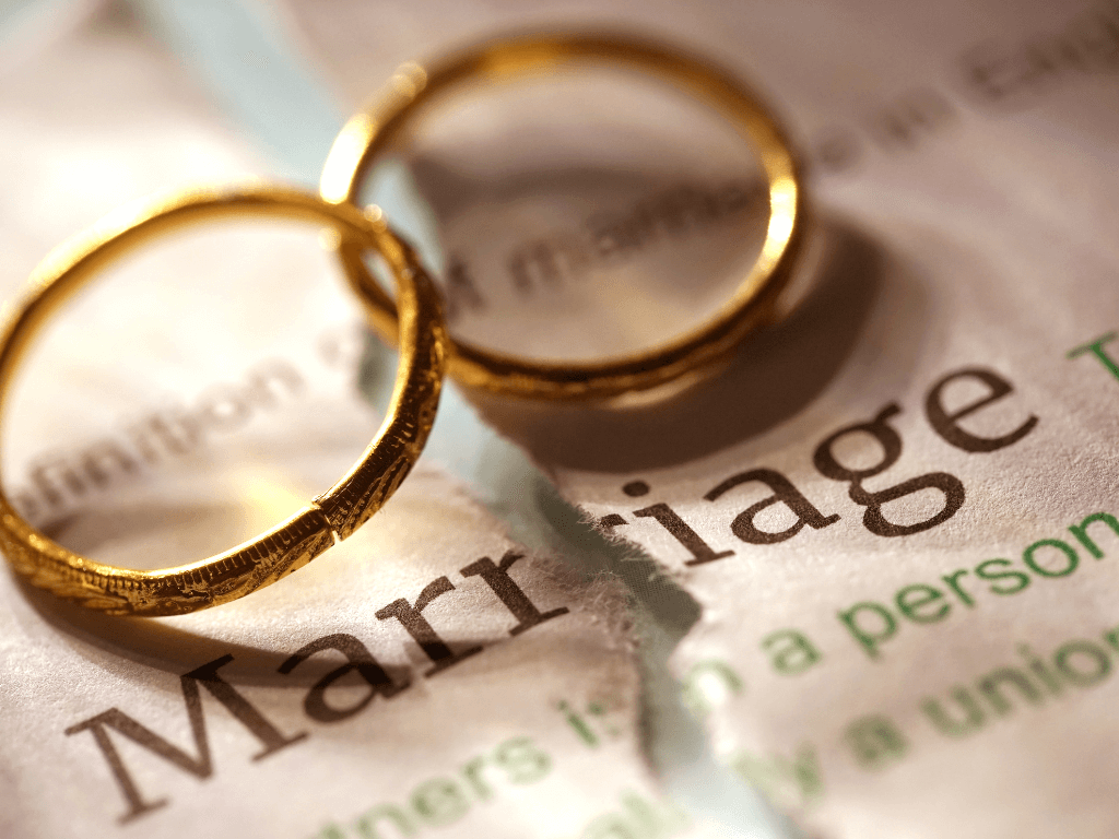 ADHD and marriage. Two wedding rings interlocked on a torn piece of paper with the word marriage written on it.