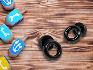 pictures of dreidels scattered on a wooden table, next to black Loop earplugs