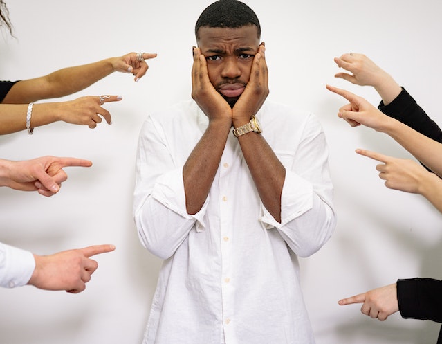 A man with ADHD and RSD standing in the middle with his hands on his phase. Fingers from all around are pointing at him.